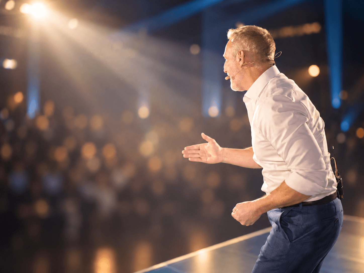 Gido Schimanski speaking on stage under warm spotlight, with the audience blurred in the foreground.